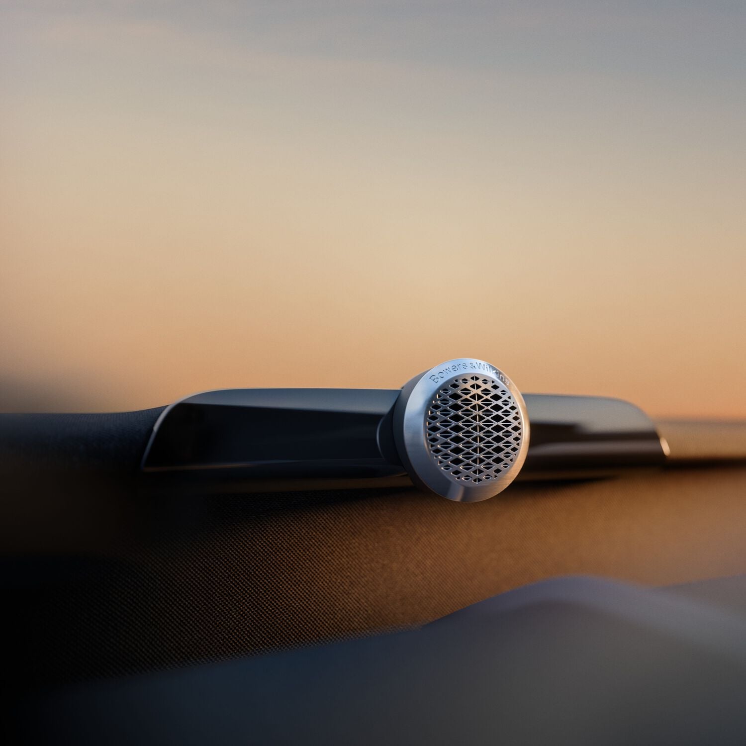 Small silver circular Bowers & Wilkins speaker with orange gradient background