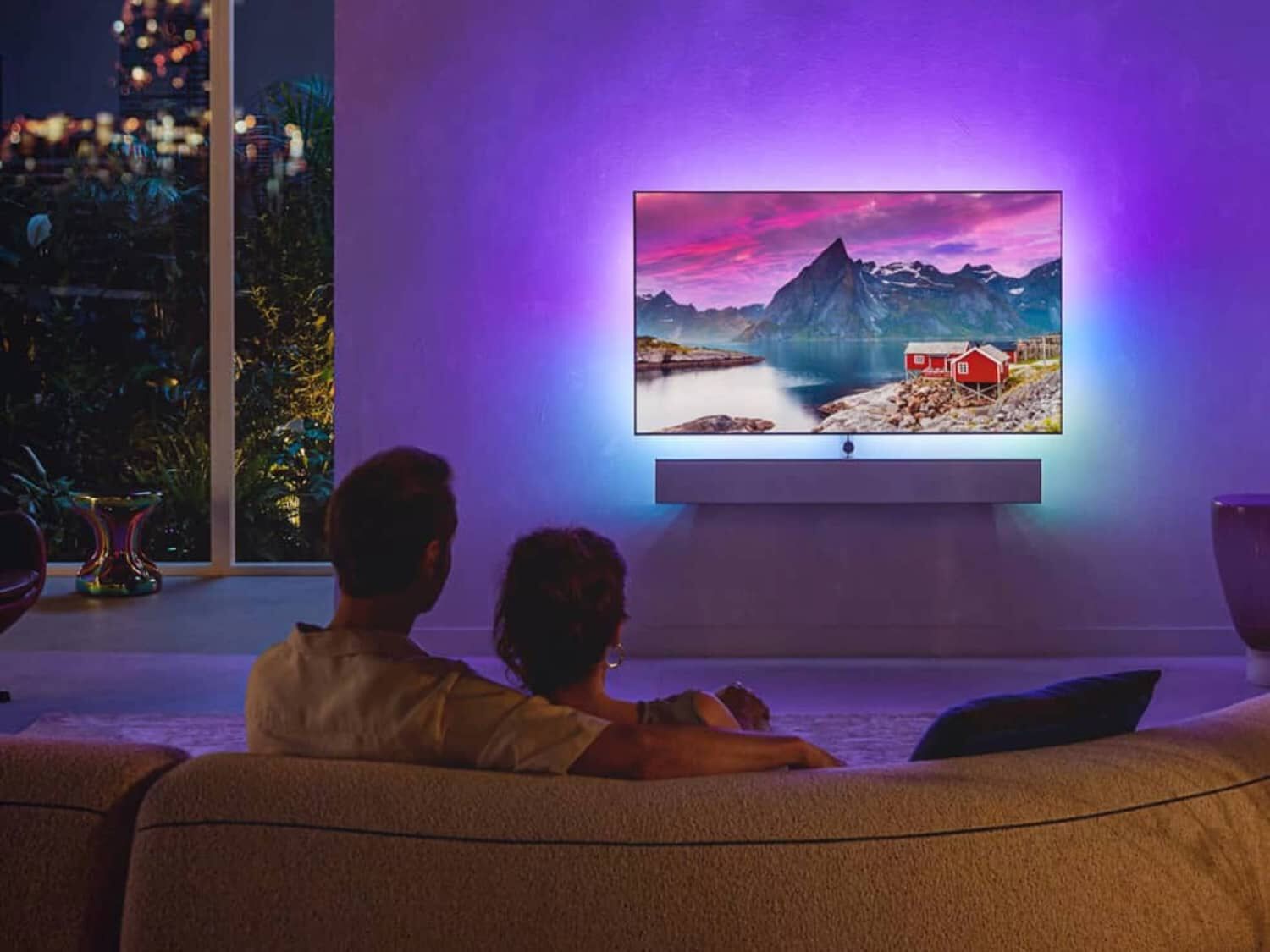 Couple sitting in living room on couch facing TV with blue and purple lights illuminating behind