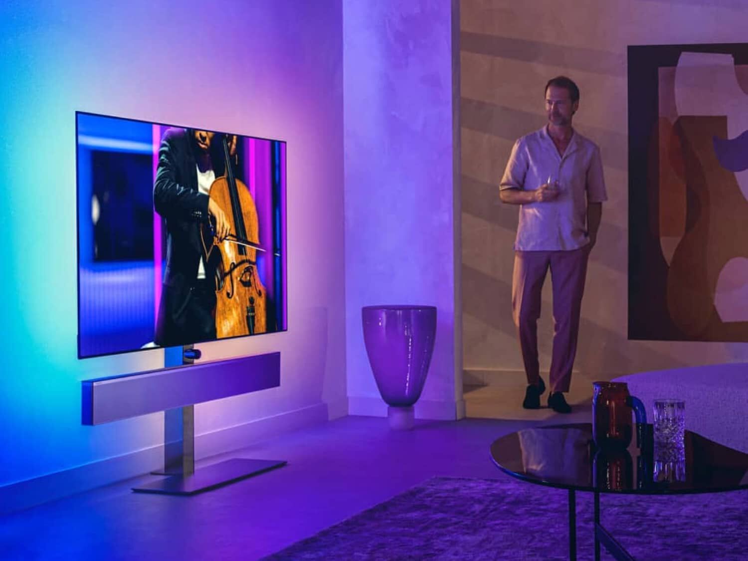Man in white shirt facing left looking at TV on floating stand with purple and blue lights behind and silver soundbar below