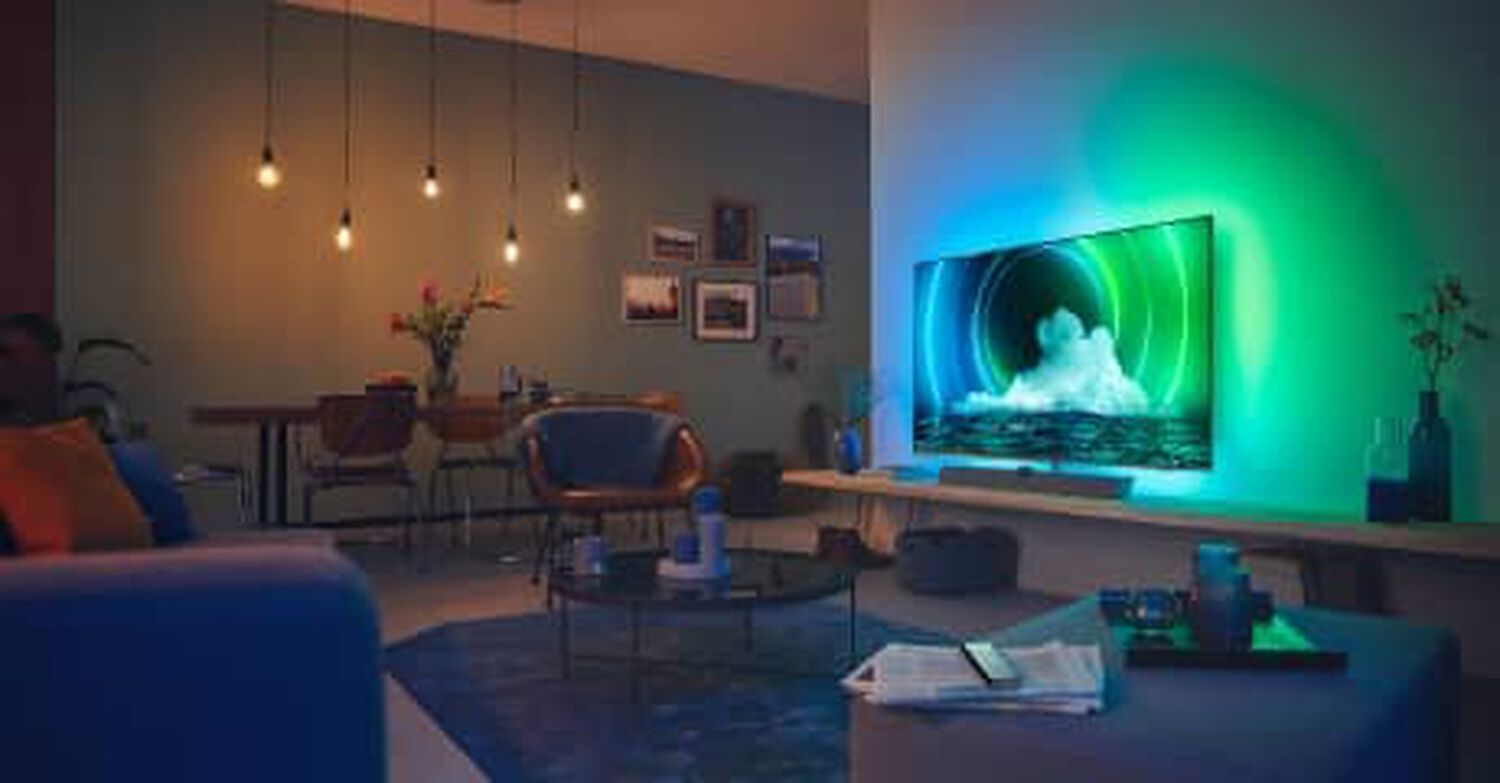 Philips OLED+9636 in living room with blue and green lights behind TV and silver soundbar below