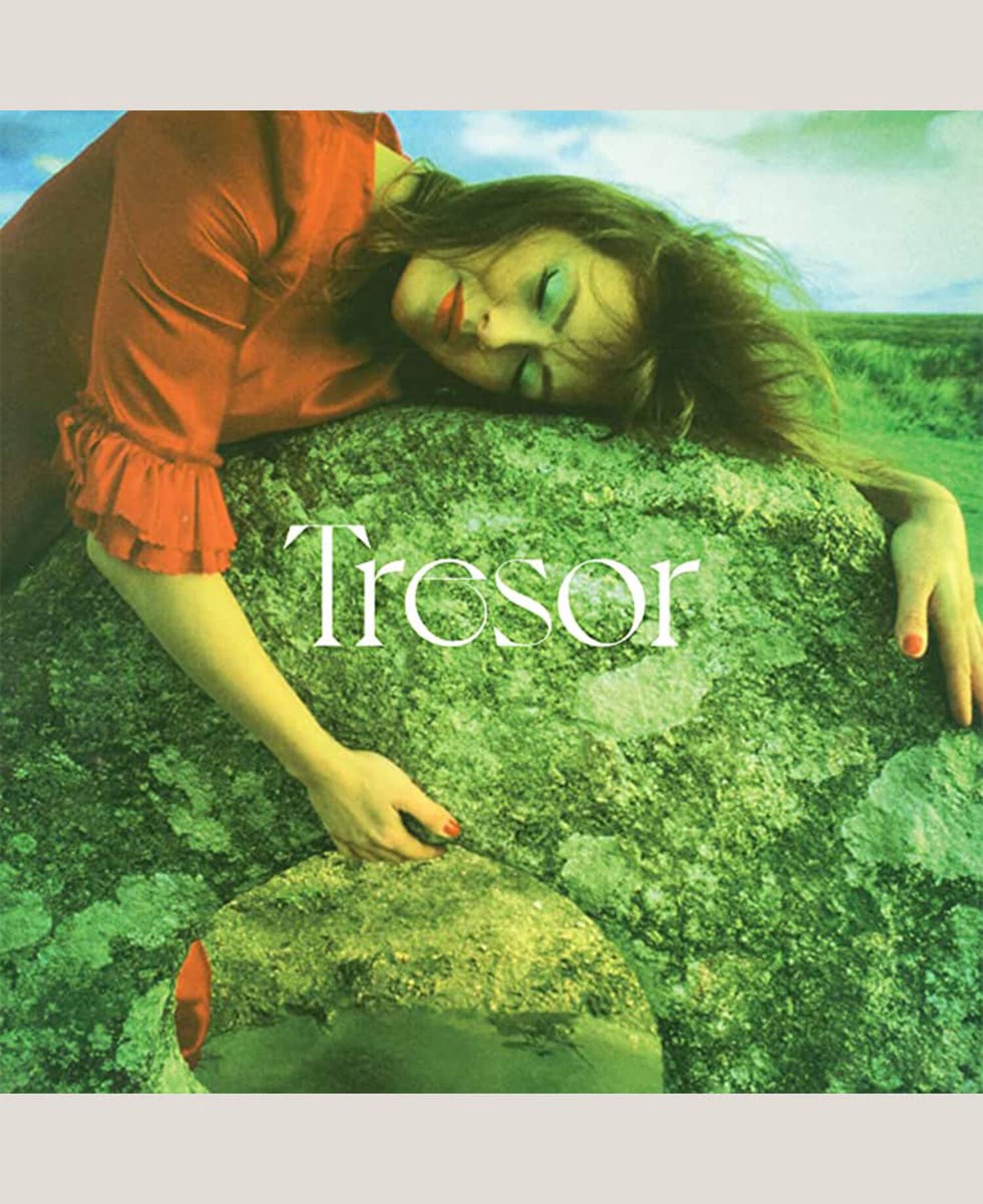 Woman in red dress laying on top of rock structure hugging it