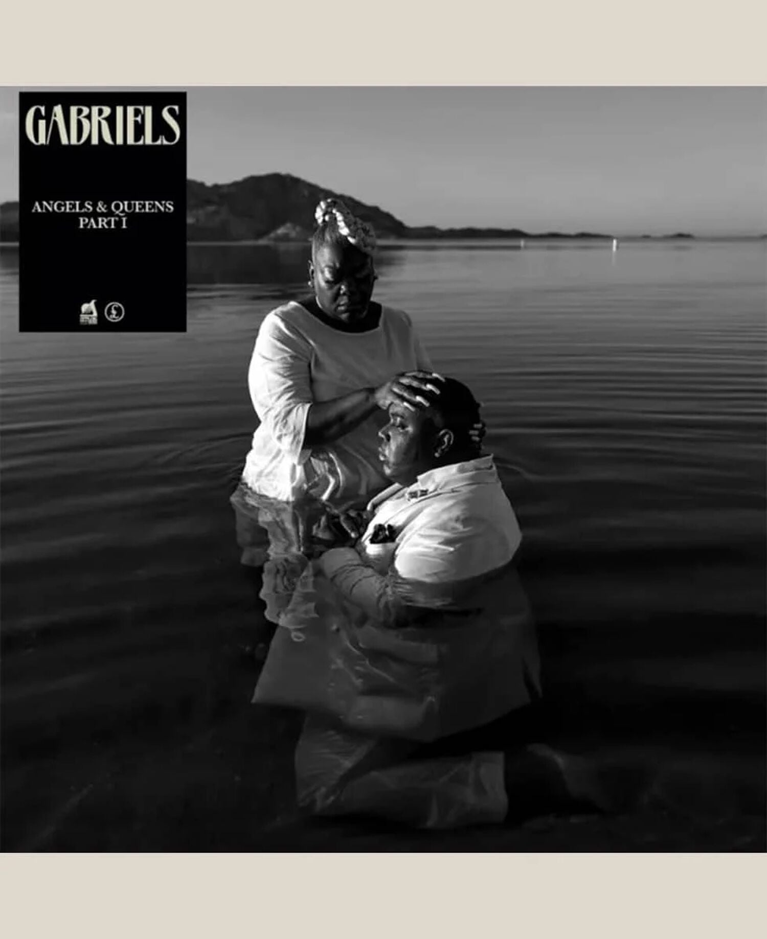 Man kneeling in body of water wearing suit with woman placing hand on his head in black & white