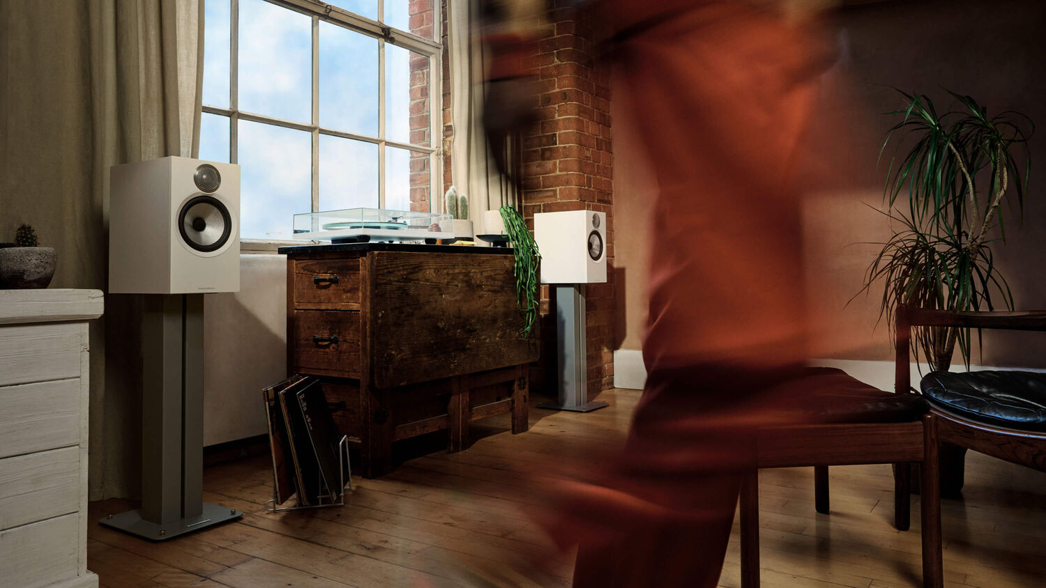 Someone quickly walking by two white 606 S3 loudspeakers with a turntable in between