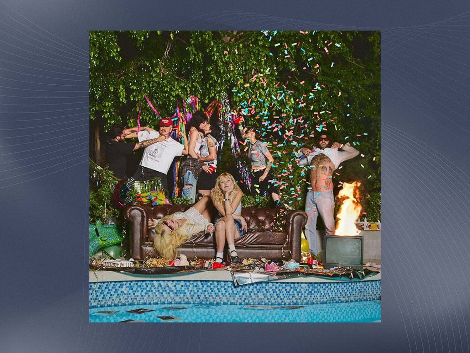 Group of men and women sitting and standing around brown couch next to pool
