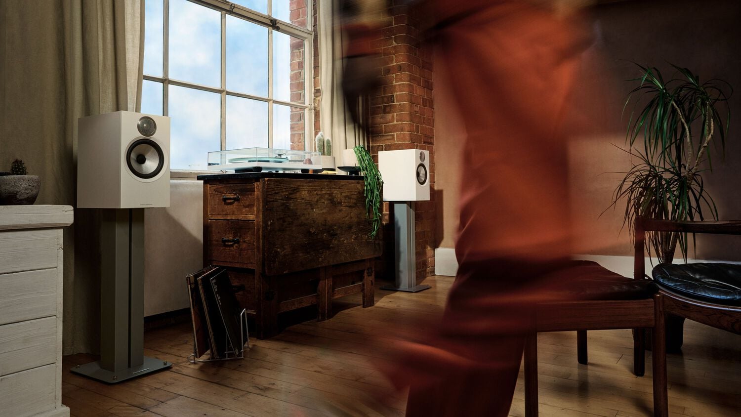 Someone quickly walking by two white 606 S3 loudspeakers with a turntable in between