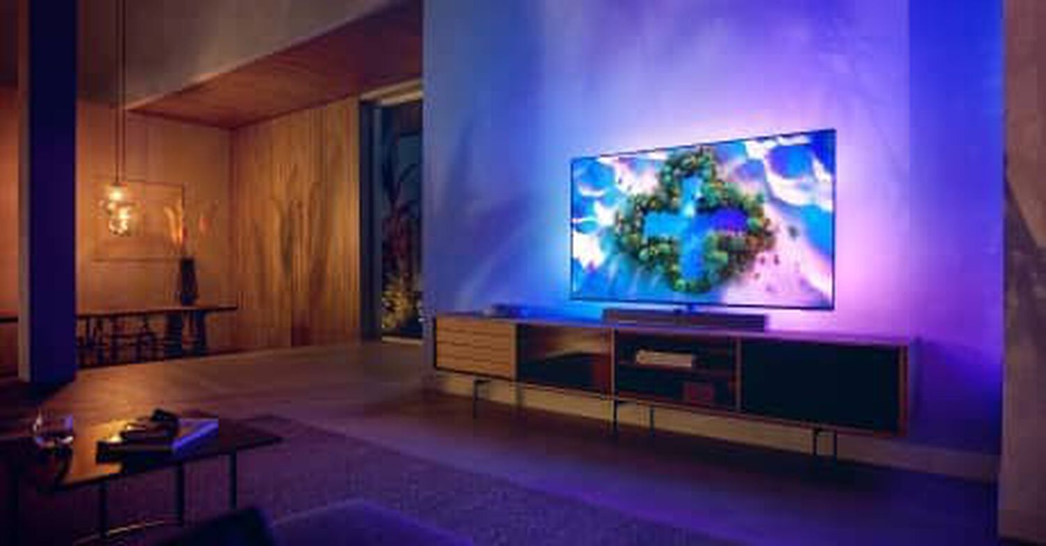 Philips OLED+936 in living room with blue and pink lights behind TV and silver soundbar below