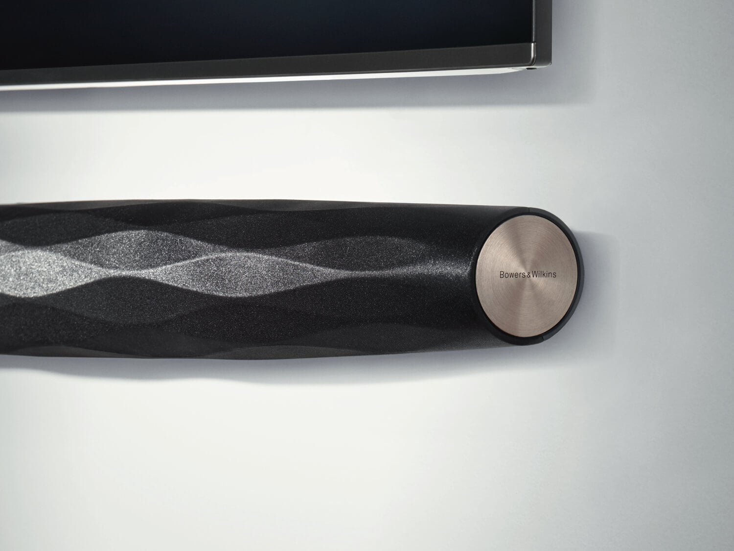 Black Bowers & Wilkins speaker mounted on wall below TV