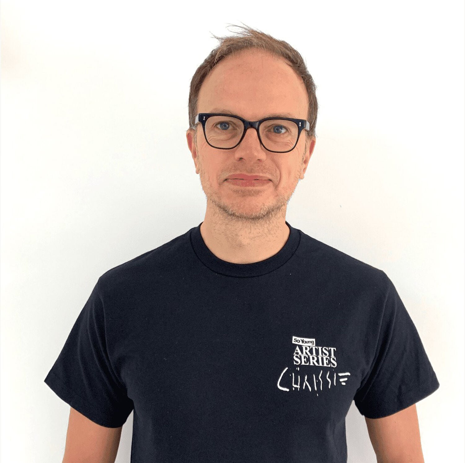 Headshot of man wearing glasses and graphic tee with white background