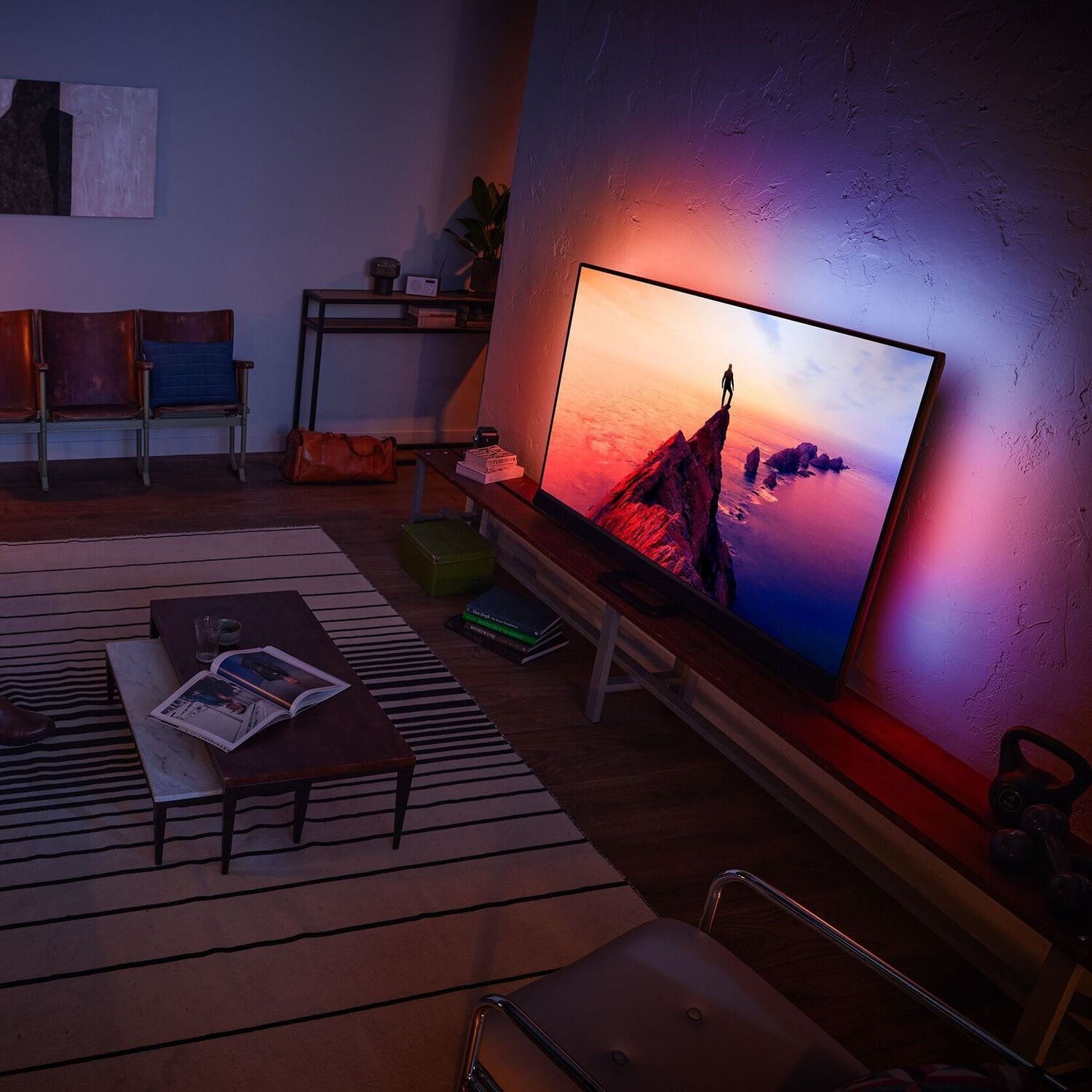 Living room with white and black rug, wood coffee table, and wood media console with illuminated TV showing a mountain with sunset