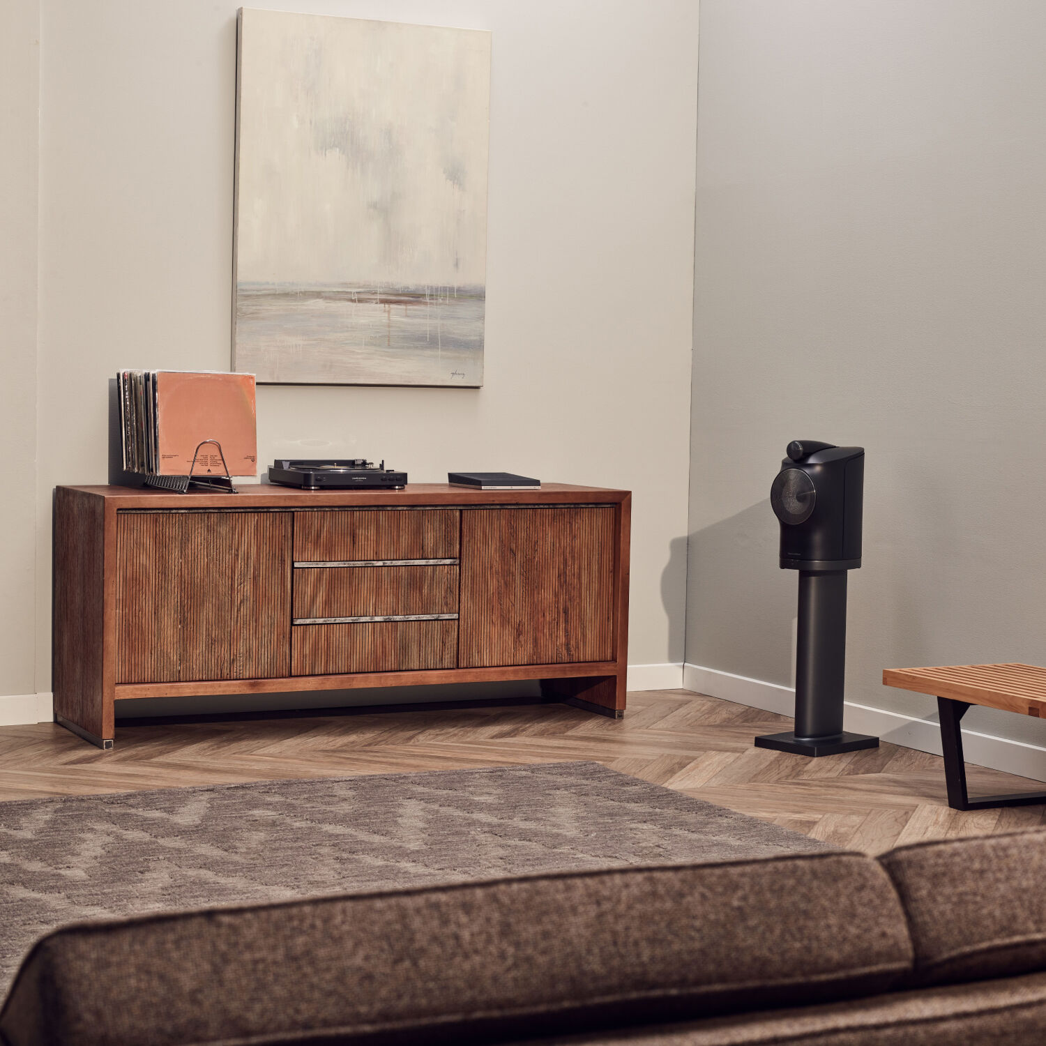 Black turntable on media console with vinyl records with black standing speaker to the right