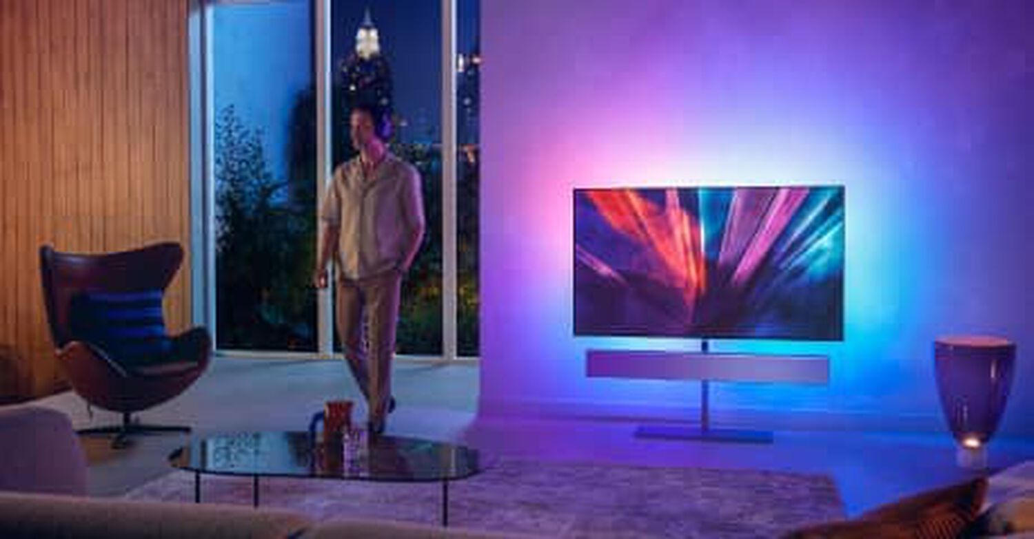 Philips OLED+986 in living room with blue, pink, purple and white lights behind TV and silver soundbar below